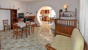 A living room with a dining table, chairs, a fireplace, and a kitchen visible through an archway. - Large apartment sleeping 9 can accommodate 2 families (Barano d'Ischia)