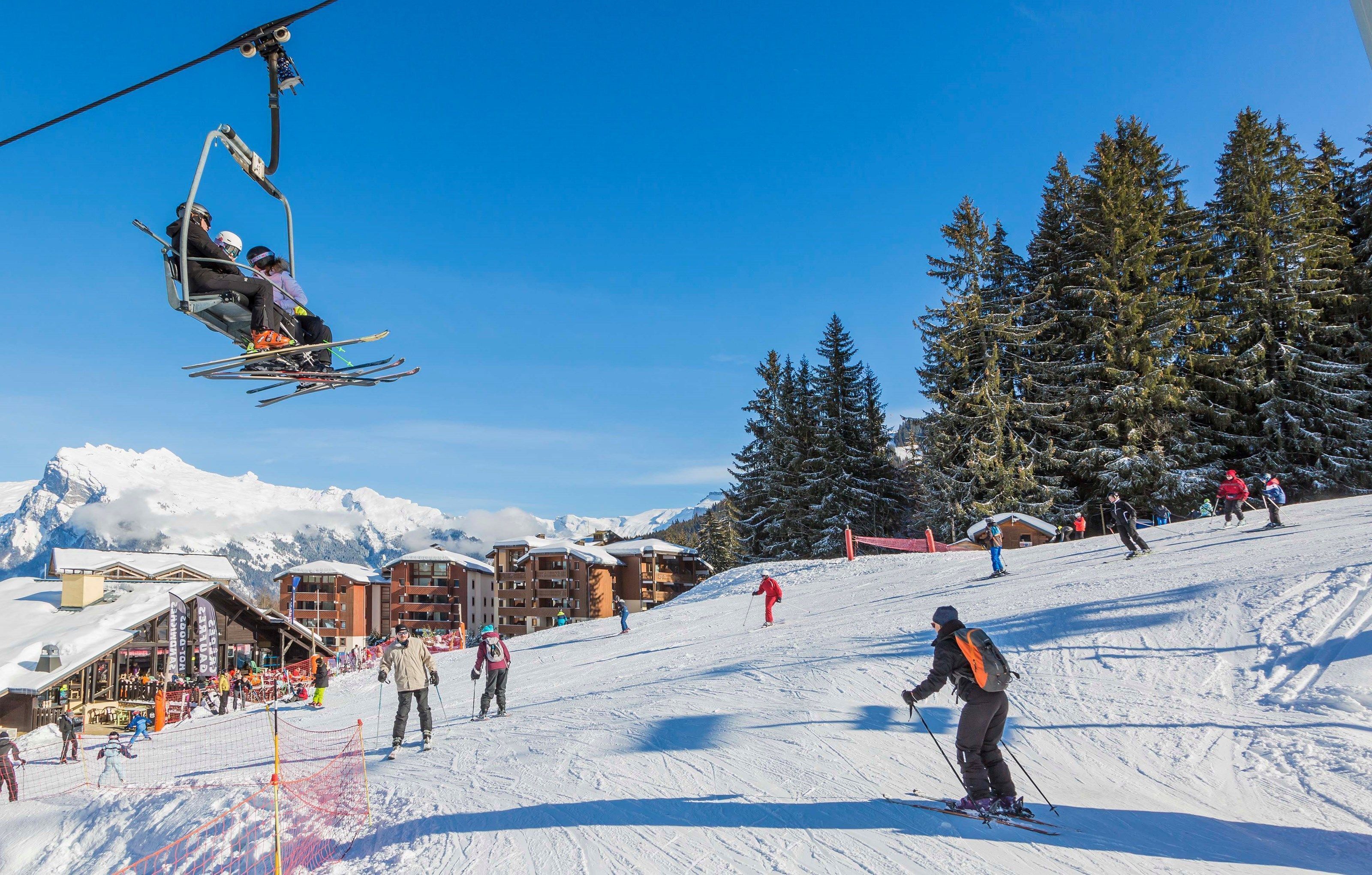 A ski resort with a ski lift, snow-covered trees, and a building with a sloped roof.