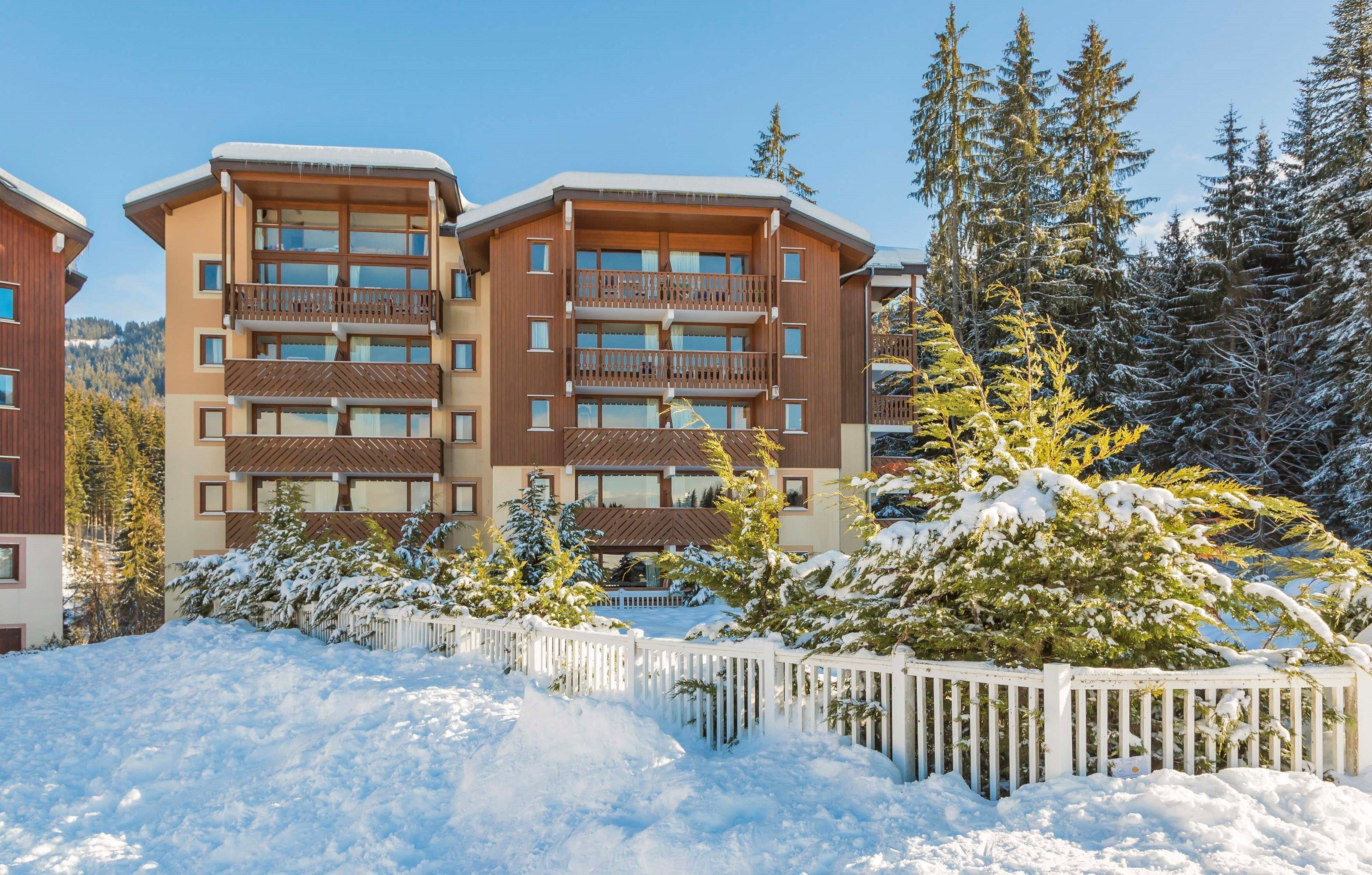 Un hôtel à plusieurs étages, doté de balcons, entouré d’arbres couverts de neige et d’une clôture blanche.