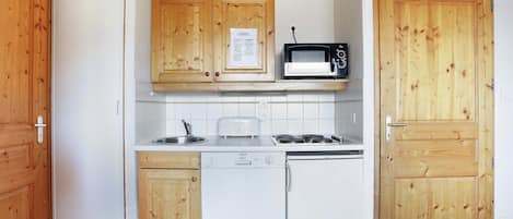 A compact kitchen with wooden cabinets, a microwave, a toaster, a dishwasher, and a refrigerator.