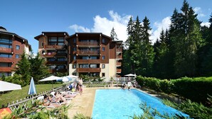 Un hotel con piscina rodeada de sillones y sombrillas, con un área boscosa al fondo.
