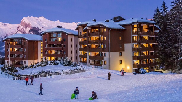Un centro de esquí cubierto de nieve con edificios de varios pisos, pistas de esquí y montañas al fondo.