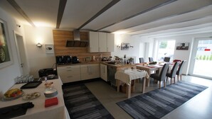 A modern kitchen with white cabinets, a dining area with a table and chairs, and a large window providing natural light. - Pension Obstgarten (Achstetten)