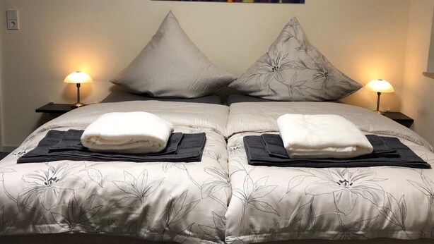 A double bed with a floral bedspread, two pillows, and two bedside lamps. - Pension Obstgarten (Achstetten)