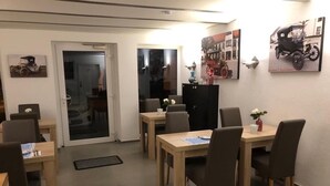 A dining area with multiple tables and chairs, a refrigerator, and wall art. - Pension Obstgarten (Achstetten)