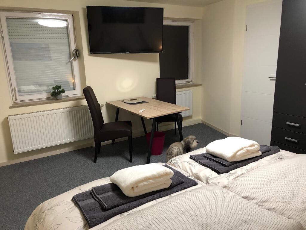 A hotel room with two beds, a desk, a chair, a TV, and a window with blinds.