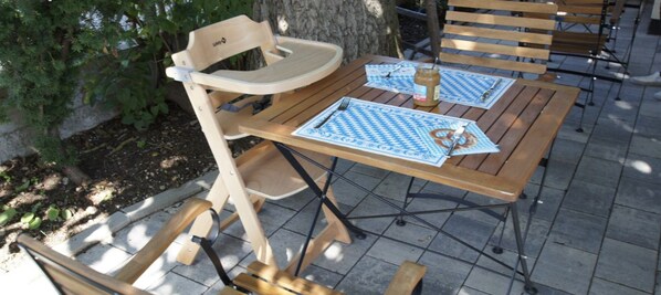An outdoor seating area with wooden tables and chairs, arranged on a tiled patio. - Pension Obstgarten (Achstetten)