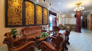 A spacious living room with a traditional wooden sofa set, a coffee table, and a decorative wall panel. - Shwe Pe Ti Hotel (Mandalay)