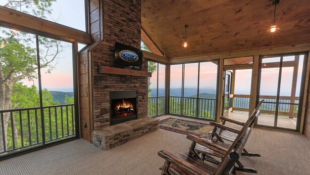 Una terraza de madera con chimenea de piedra, un televisor montado en la pared y vistas a las montañas.