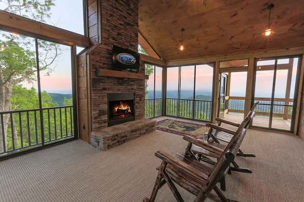 Una terraza de madera con chimenea de piedra, un televisor montado en la pared y vistas a las montañas.