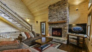 Un interior de cabaña acogedor con chimenea de piedra, un televisor y una escalera.