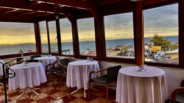 A terrace with tables and chairs, overlooking a coastal cityscape during sunset. - Terrace Guesthouse (Istanbul)