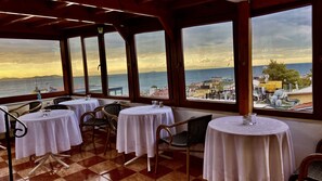 A terrace with tables and chairs, overlooking a coastal cityscape during sunset. - Terrace Guesthouse (Istanbul)