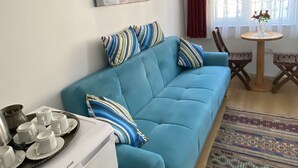 A living room with a blue sofa, striped pillows, a small table with a vase, and a decorative rug. - Terrace Guesthouse (Istanbul)
