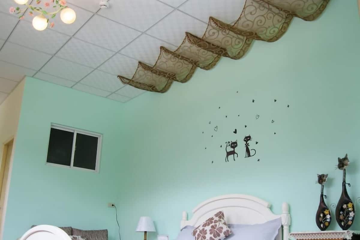Un dormitorio con cama, mesita de noche, lámpara y decoración de gatos y corazones.