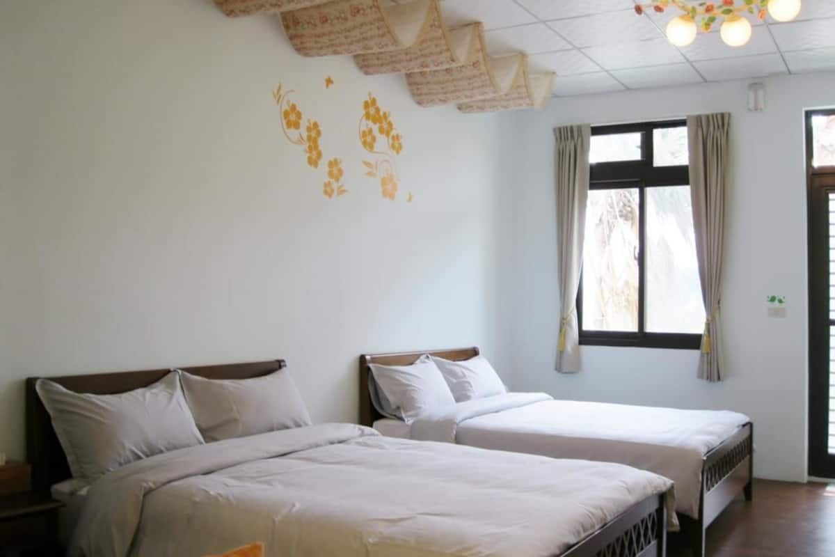 Una habitación con dos camas, un ventanal con cortinas y una lámpara en el techo.