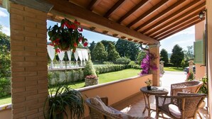 A covered patio with wicker furniture, a view of a well-manicured garden, and a brick wall. - Il Poggiolo (Camaiore)
