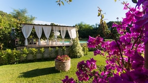 A garden with a white gazebo, a stone planter with flowers, and bougainvillea vines. - Il Poggiolo (Camaiore)