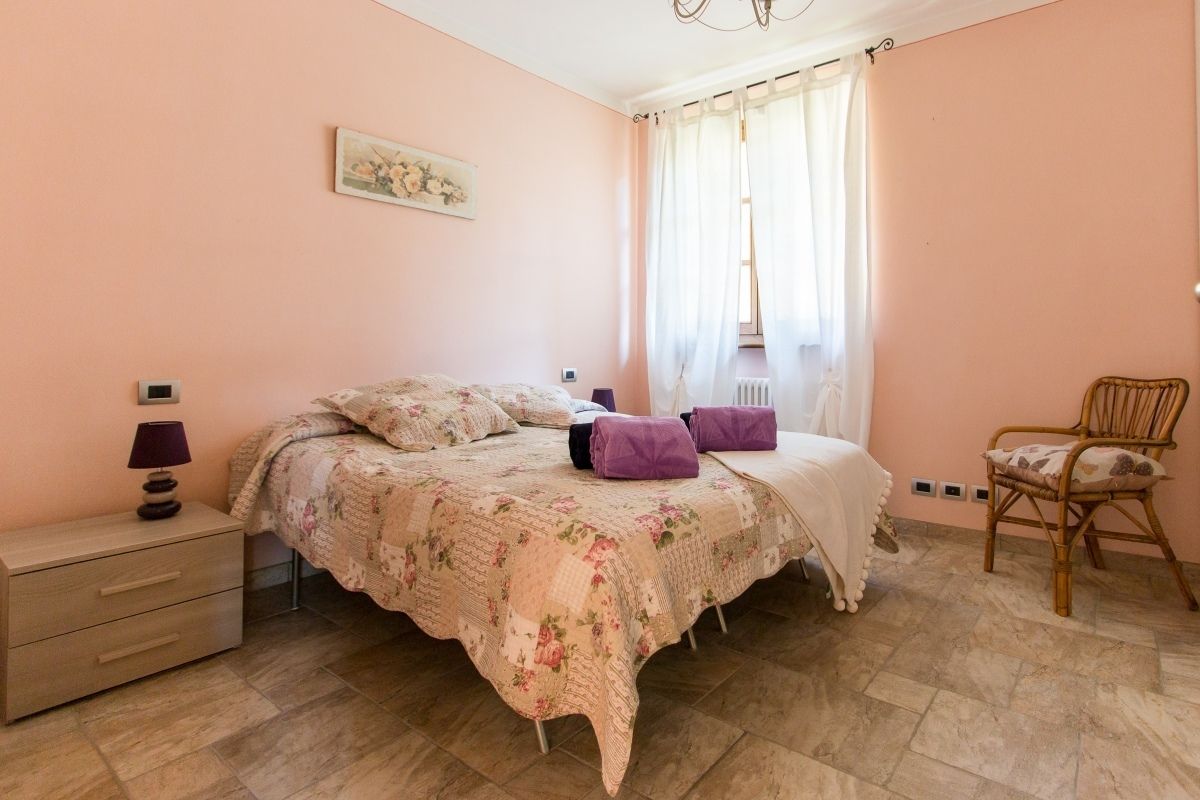 A bedroom with a bed, a chair, a nightstand, and a window with curtains.