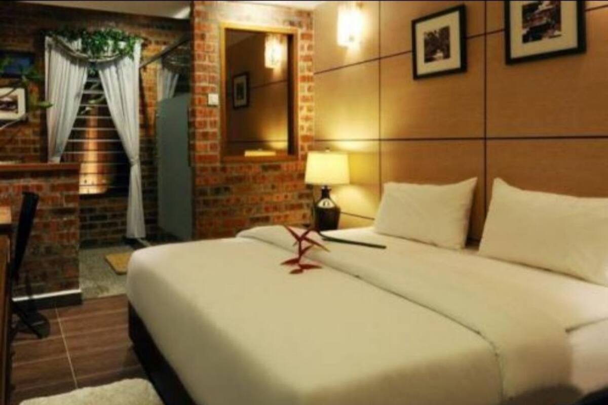 A hotel room with a large bed, a nightstand with a lamp, a brick wall, and a staircase with curtains.