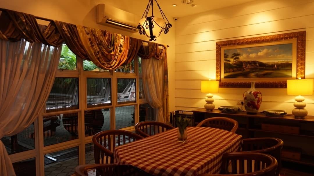 Un coin repas avec une nappe à carreaux, des chaises en bois, un lustre et un tableau accroché au mur.