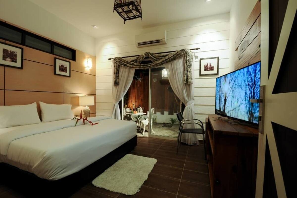 A hotel room with a large bed, a television, and a balcony with curtains.