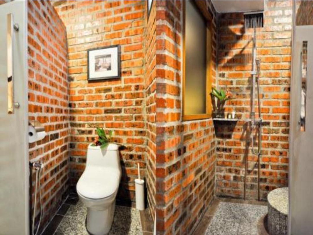 A bathroom with a brick wall, a toilet, a sink, and a shower.