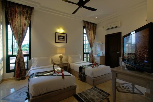 Habitación de hotel con dos camas, televisor, ventilador de techo y ventana con cortinas.