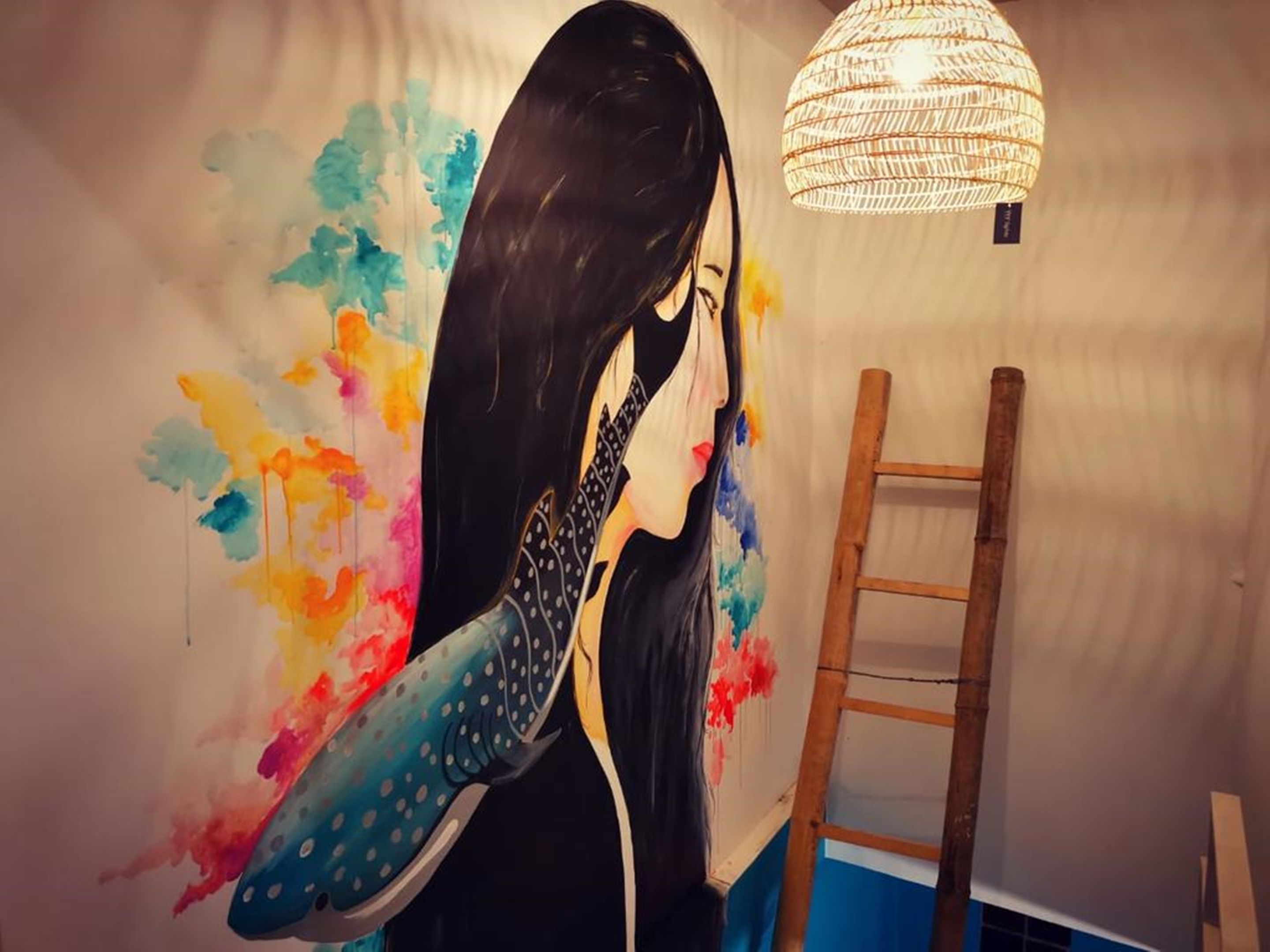 A room with a mural of a woman holding a guitar, a wooden ladder, and a hanging light fixture.