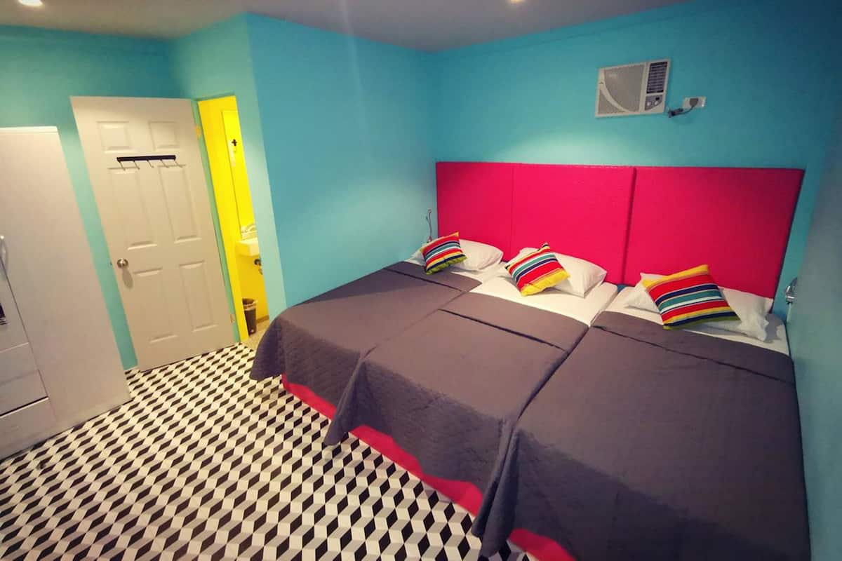 Una habitación con una cama, un armario blanco, una puerta de baño y una unidad de ventilación en la pared.