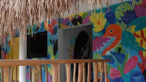 A room with colorful murals, a thatched roof, and a patterned floor. - Way Shack Hostel (Oslob)