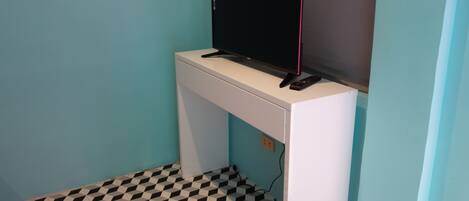 A small room with a white desk, a black monitor, and a remote control on it. The floor has a black and white checkered pattern.