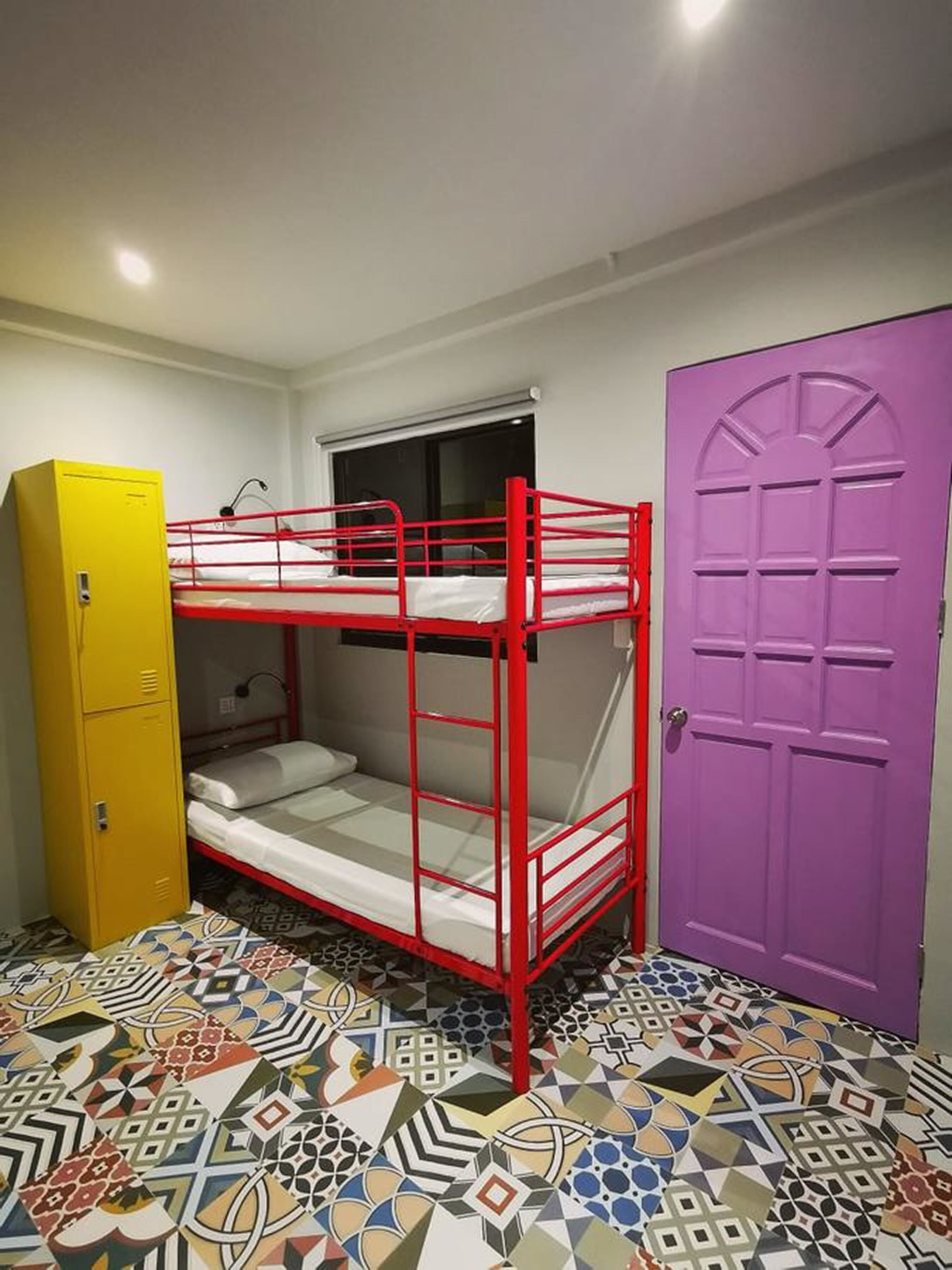 Habitación con literas, un armario amarillo, una puerta morada y un suelo estampado.