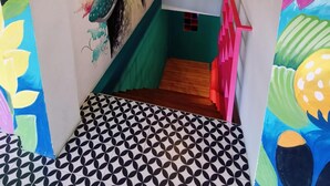 A narrow hallway with a colorful mural on the walls, a patterned floor, and a hanging light fixture. - Way Shack Hostel (Oslob)