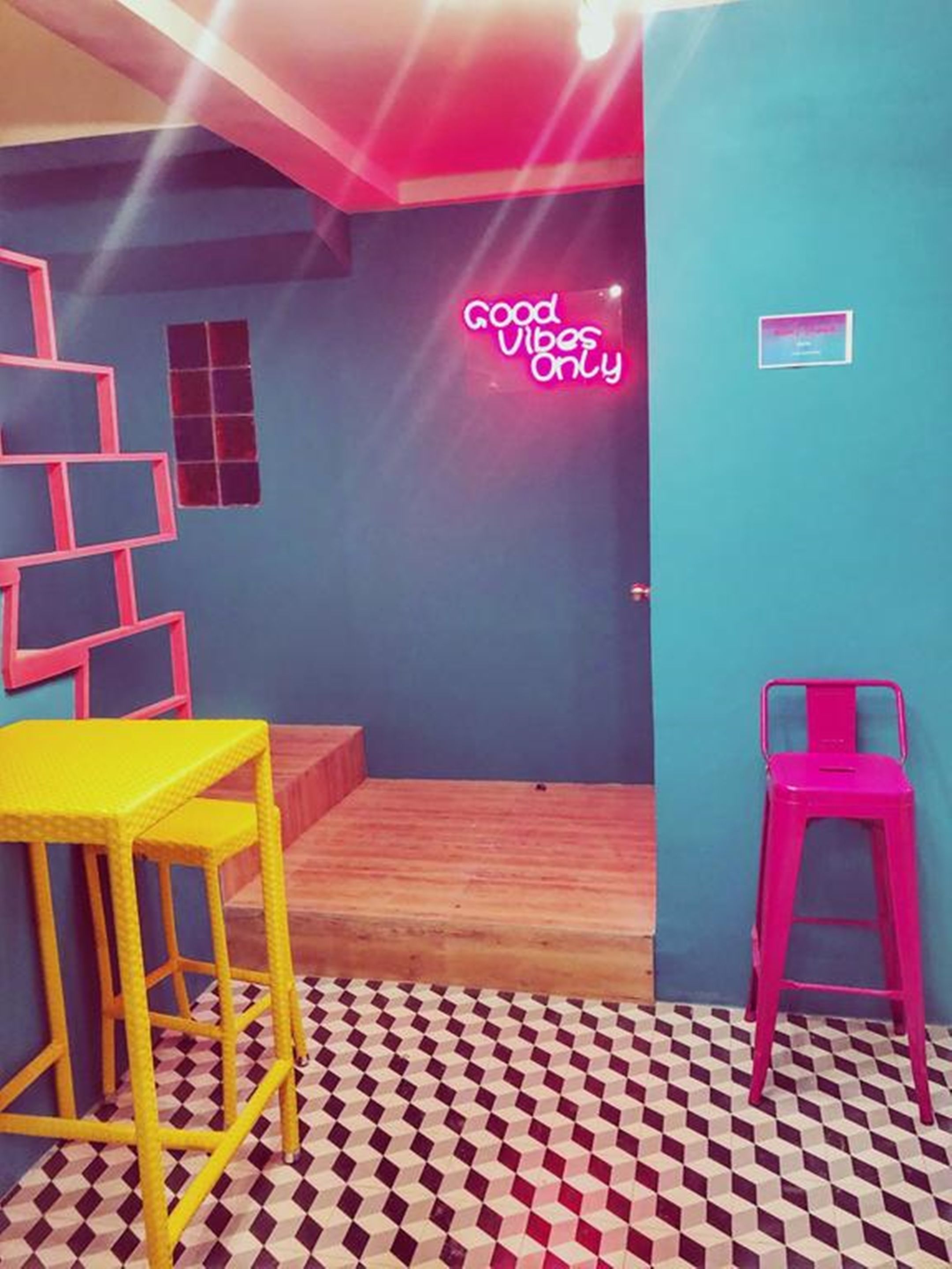 Una habitación con piso a cuadros, un letrero de neón que dice "good vibes only" y una escalera que sube a un nivel superior.