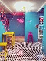 Una habitación con piso a cuadros, un letrero de neón que dice 'Good Vibes Only', un refrigerador y una escalera con marcos rosas.