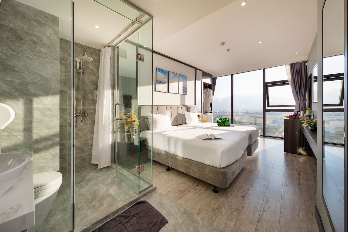 Une chambre d’hôtel moderne dotée d’un grand lit, d’une douche en verre, d’une vue sur la ville et d’une grande fenêtre.