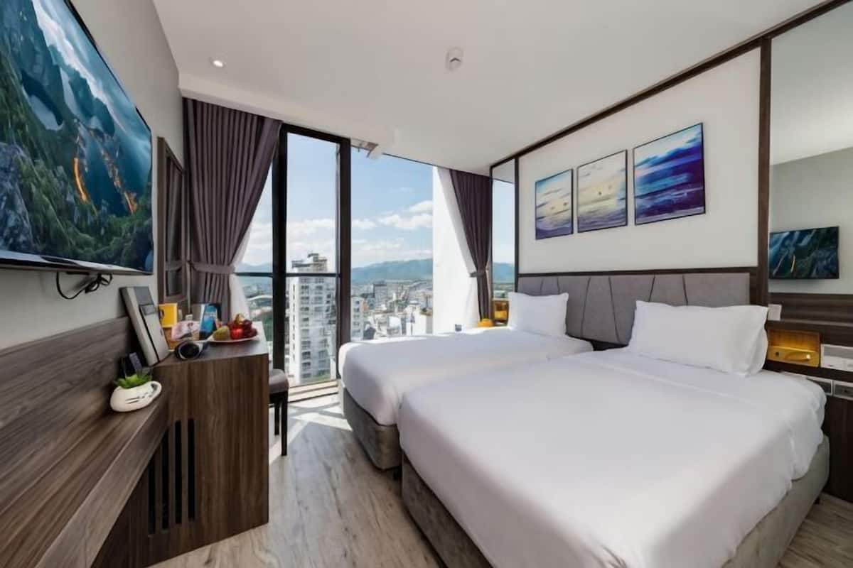 Une chambre d’hôtel avec deux lits, un bureau, une télévision et une grande fenêtre donnant sur la ville.