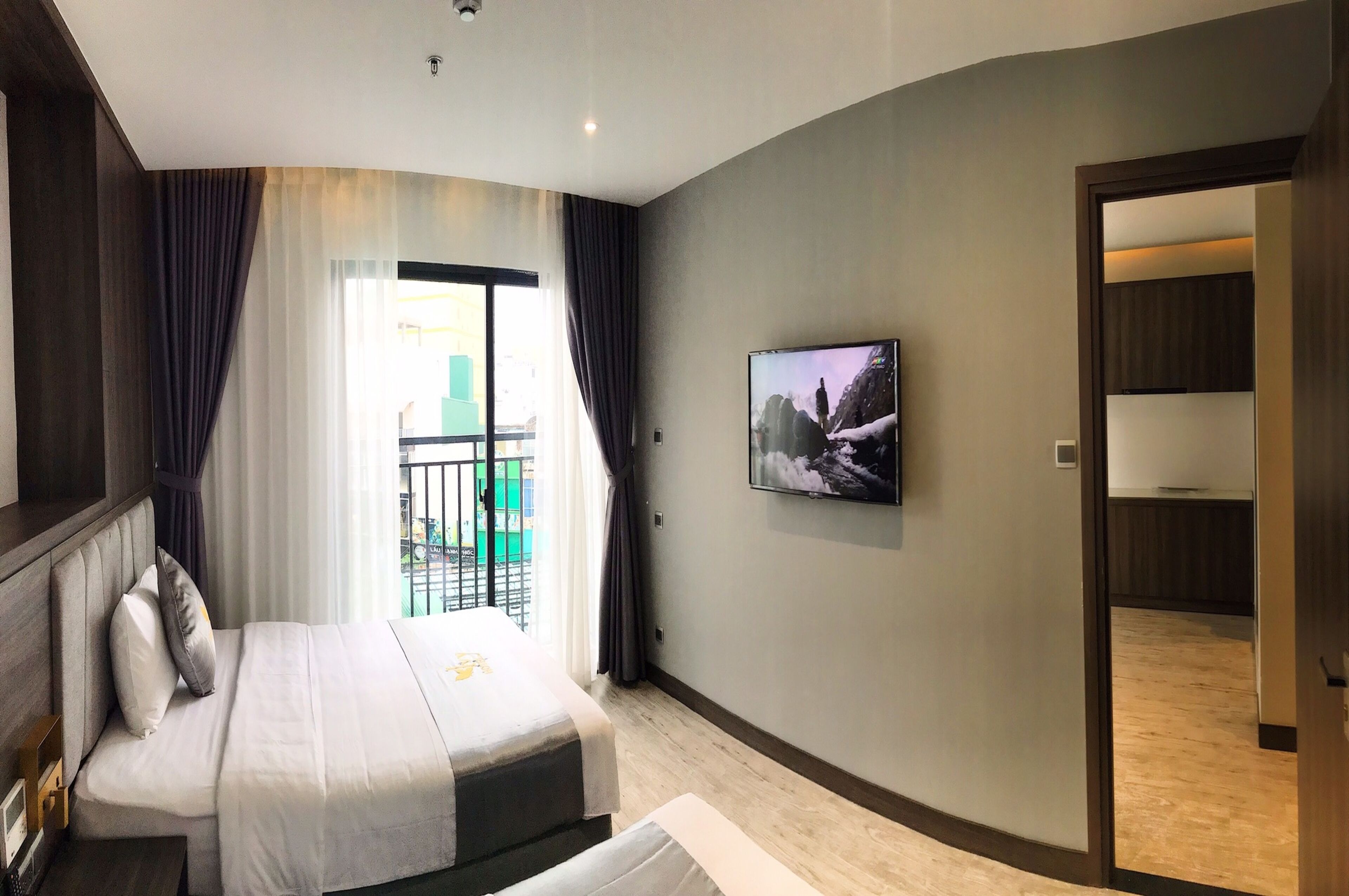 Una camera d'albergo moderna con un letto, una TV a parete e un balcone con vista sugli edifici.