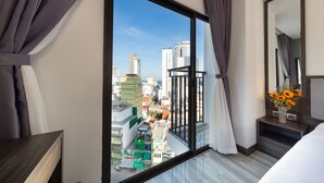 Hotelkamer met een groot raam met uitzicht op de stad, een bed, nachtkastje en spiegel.