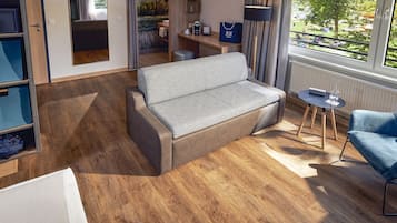 A modern hotel room with a grey sofa, a blue armchair, and a small table with a lamp.