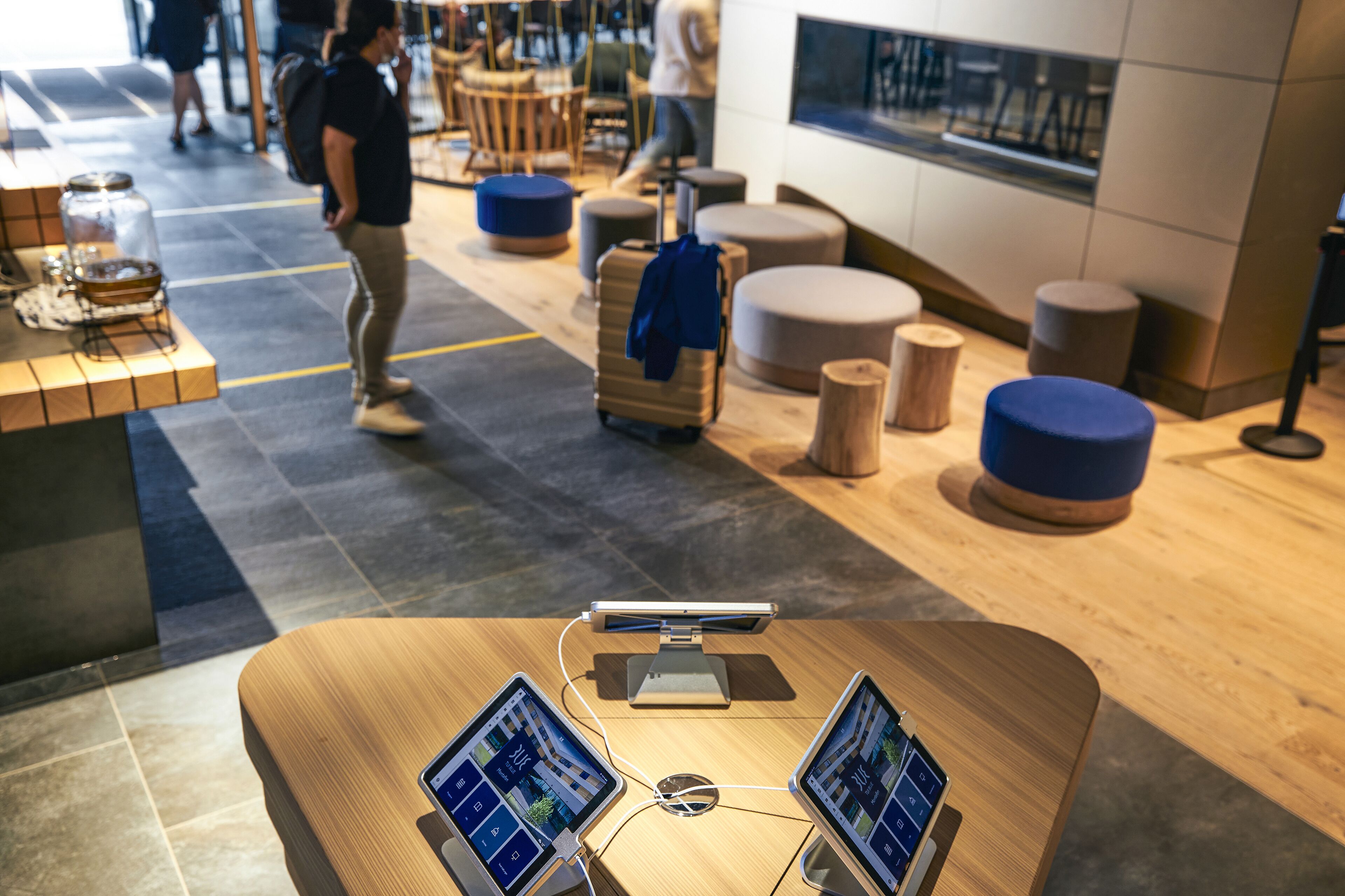 Un moderno vestíbulo de hotel con un mostrador de recepción de madera, dos monitores y un quiosco digital.