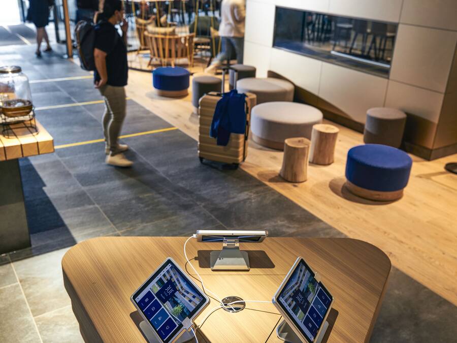 Un moderno vestíbulo de hotel con un mostrador de recepción de madera, dos monitores y un quiosco digital.