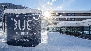 A snow-covered sign with "Blue TUI Montafon" text, a modern building with glass windows, and a snowy landscape. - TUI BLUE Montafon (Tschagguns)