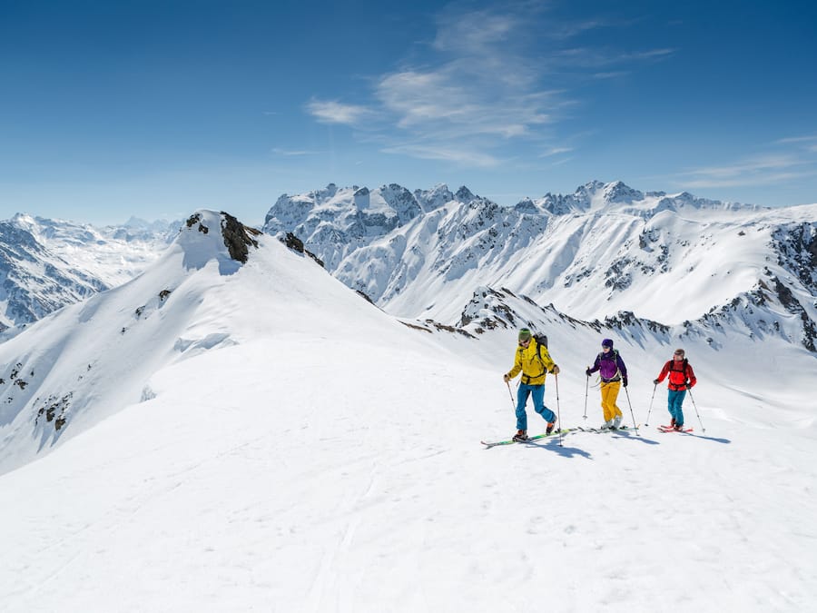 Paisatge nevà d'una muntanya amb tres esquiadors.