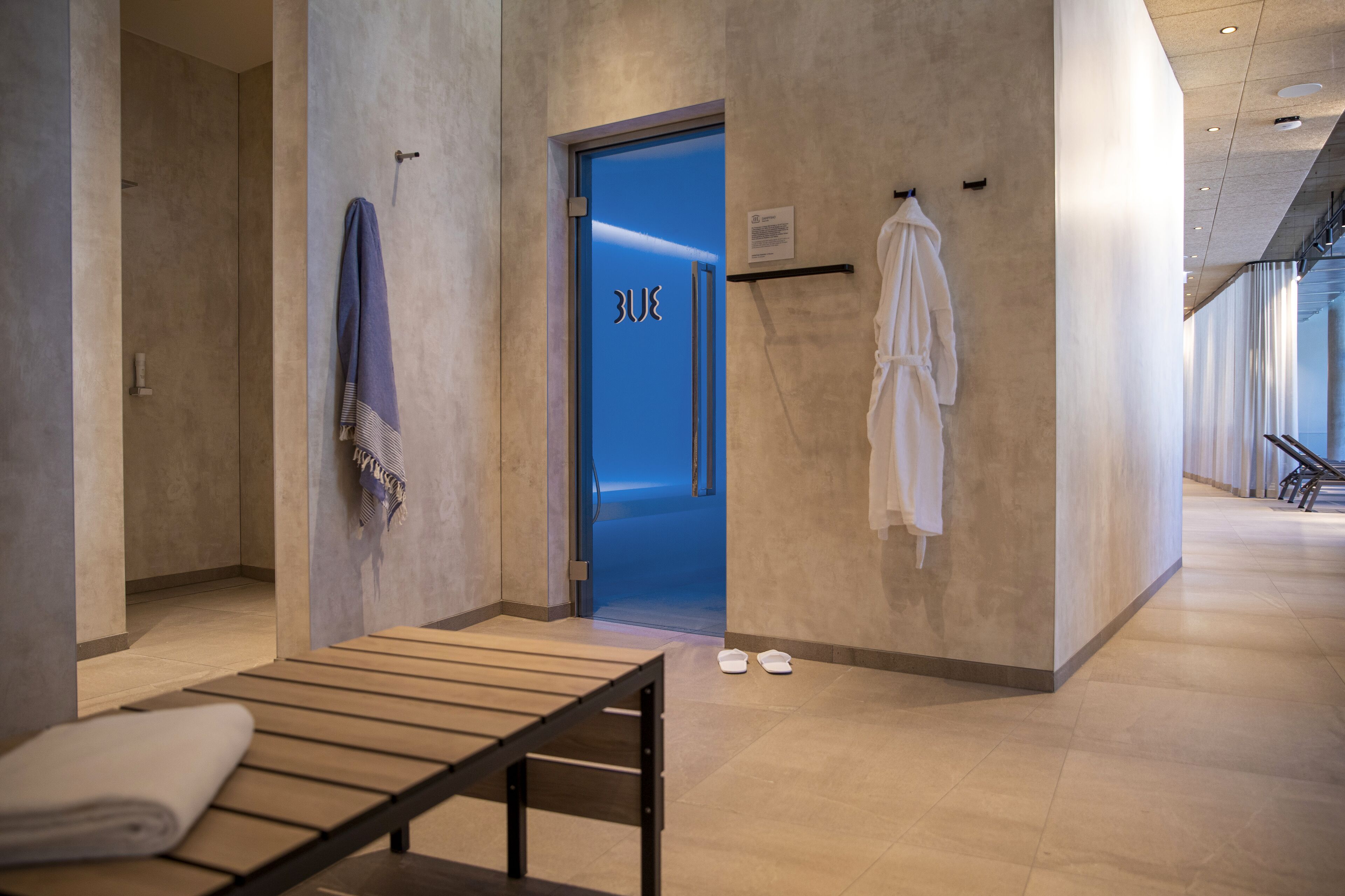 Ein moderner Wellnessbereich mit einer Bank, Handtüchern und einer blauen Tür.