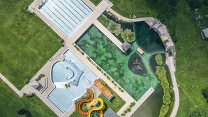 An aerial view of a park with a swimming pool, water slides, and a small bridge. - TUI BLUE Montafon (Tschagguns)