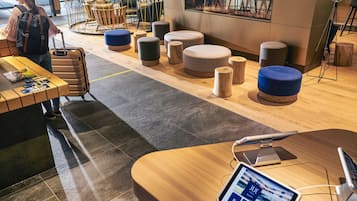 A hotel lobby with a wooden reception desk, a seating area with ottomans, a luggage cart, and a modern interior design.