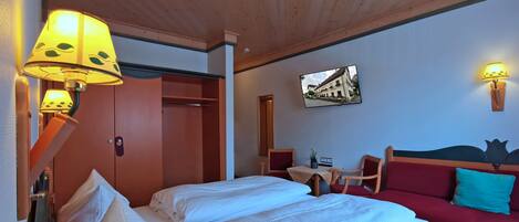 Habitación de hotel con cama, dos lámparas de noche, un sofá rojo, una mesita y televisor montado en la pared.