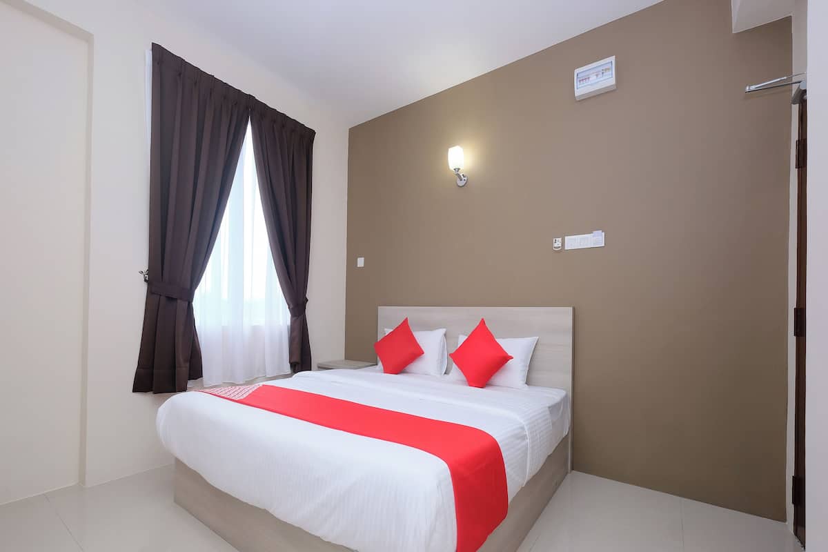 A hotel room with a bed, curtains, a wall-mounted light, and a door.